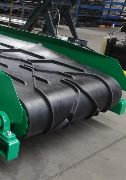 Close-up van een zwarte rubber transportband met visgraatprofiel op groen frame